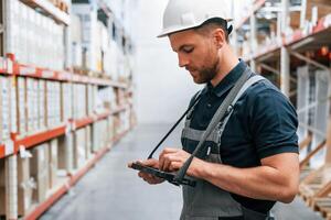 Checking data in the tablet. Employee in uniform is working in the storage at daytime. photo