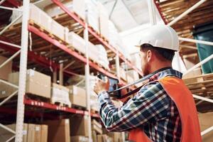 Holding tablet in hands. Employee in uniform is working in the storage at daytime. photo