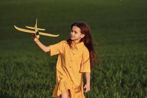Running forward with toy plane. Happy girl have a walk outdoors on the field at summer photo