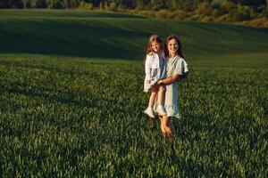 Standing and posing for a camera. Mother and daughter have fun outdoors on the field at summer. photo