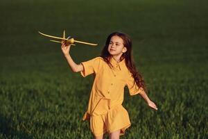 Running forward with toy plane. Happy girl have a walk outdoors on the field at summer., photo