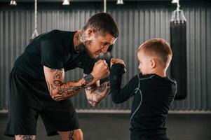 Man is helping kid with learning and practicing. Coach is teaching the boy box techniques indoors.. photo
