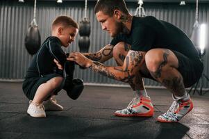 Man is helping kid with learning and practicing.. Coach is teaching the boy box techniques indoors photo