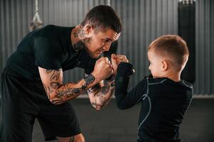 Man is helping kid with learning and practicing.., Coach is teaching the boy box techniques indoors photo