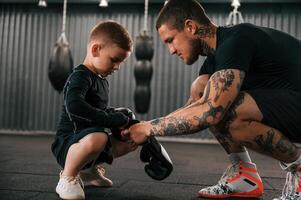 Man is helping kid with learning and practicing. Coach is teaching the boy box techniques indoors photo