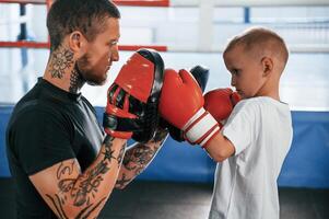 How to punch correct way., Coach is teaching the boy box techniques indoors photo