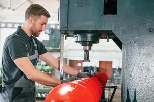 Measuring red colored sharp part. Man in uniform is in workstation developing details of agriculture technique.. photo