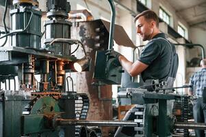 Standing by metal processing device. Man in uniform is in workstation developing details of agriculture technique photo