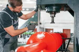 Measuring red colored sharp part. Man in uniform is in workstation developing details of agriculture technique photo