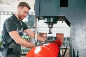 Measuring red colored sharp part. Man in uniform is in workstation developing details of agriculture technique.,. photo
