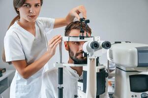 Man's vision checked by female doctor in the clinic by using special optometrist device photo