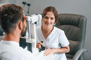 Modern technologies.. Man's vision checked by female doctor in the clinic by using special optometrist device photo