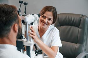Modern technologies. Man's vision checked by female doctor in the clinic by using special optometrist device photo