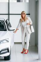 Going to the automobile. Woman in white formal clothes is in the car dealership photo