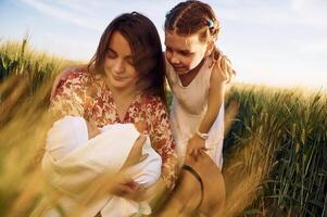 Looking at the newborn baby.. Mother with girl is on the field at sunny day together photo