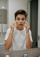 boy applying face cream in front of mirror on bathroom. Teenager Applying Face Cream photo