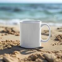 A blank white mug resting on sandy beach, with ocean waves in the background. photo