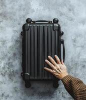 Black Carry-On Suitcase and Elderly Hand on Gray Surface photo