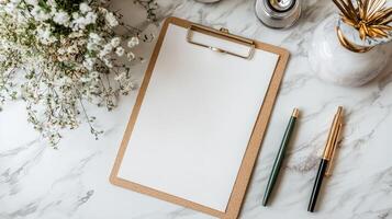 Blank clipboard on marble table with flowers and vases photo