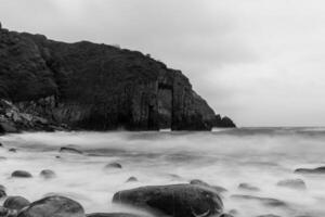 Misty sea surrounding rocky coastline with natural arch in black and white photo
