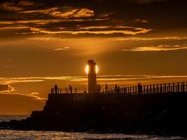 People walking on pier at sunset near lighthouse in scotland photo