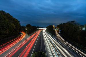 Highway traffic at dusk showing red and white light trails with green forest on each side photo