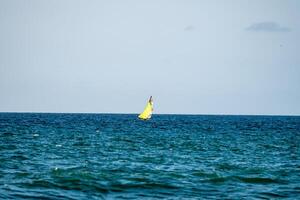 Small yellow sailboat sailing in the ocean off newquay beach photo