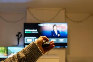 Man using remote control, changing channels on television, watching news photo