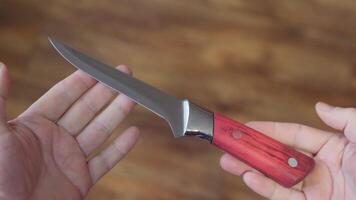 A sharp knife with a metal blade and wooden handle held in hands. video
