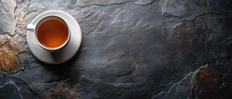 Top View of Tea in White Porcelain Cup Placed on Dark Slate Stone Background with Copy Space photo