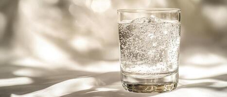 Close up of a glass filled with sparkling mineral water and ice reflecting golden sunlight on a silky surface photo