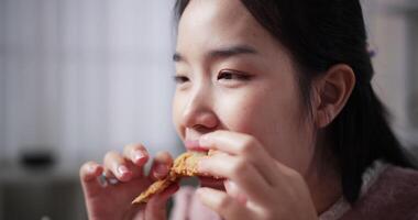 Handheld selective focus shot, Face of Beautiful woman happily bites fried chicken wings and eats them on a dining table at home. video