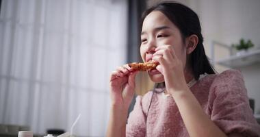 Handheld low angle view shot, Beautiful woman happily bites fried chicken wings and eats them on a dining table at home. video