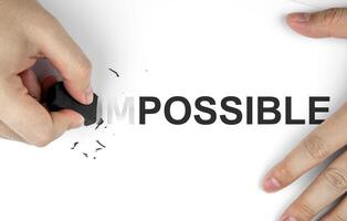 Top view of hand using eraser to erase the word IM in front of word POSSIBLE on paper to change the meaning. Business mindset concept, inspiration and determination to make your goals successful. photo