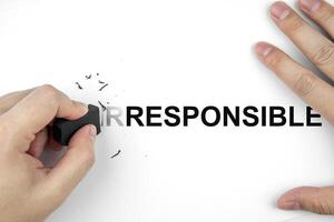 Top view of hand using eraser to erase the word IR in front of word RESPONSIBLE on paper to change the meaning. Concept of development, efficiency improvement, and Corporate Social Responsibility CSR photo