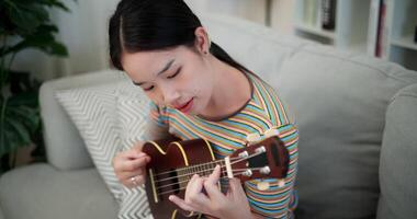 Handheld high angle view shot, Happy woman playing ukulele on sofa in relaxing and warm atmosphere in living room at home. Enjoying the moment. video