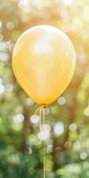 Yellow balloon floating in sunny garden with greenery and soft bokeh background photo