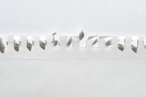 Close-up of torn white paper with perforated edge and folded tabs against light background. photo