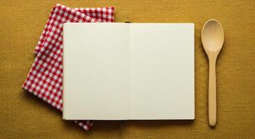 A notebook, a spoon and a red gingham napkin on a yellow background photo