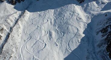 An aerial view of a mountainous landscape covered in snow, showing intricate patterns created by recent avalanches photo