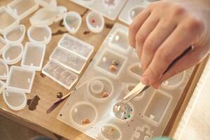 Close up of hand working with resin molds and small objects for jewelry crafting project. photo