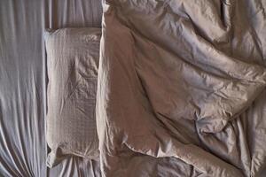 Empty unmade bed with wrinkled sheets and pillow in neutral tones depicting relaxation and home comfort. photo
