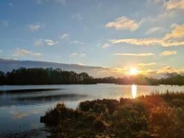 Sunset reflecting on calm lake with cloudy sky and trees silhouette photo