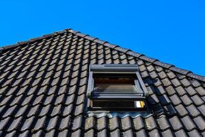 Open roof window on a tiled roof under blue sky photo