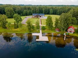Riga, Latvia, 2024 - Lakeside View with Wooden Dock and Modern House in Forested Area photo