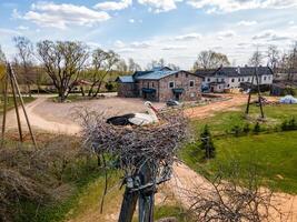 Riga, Latvia, 2024 - Stork Nest on Tall Pole with Rustic Buildings in Countryside photo