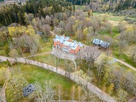 Riga, Latvia, 2024 - Aerial View of Historic Brick Mansion in Temperate Forest Setting photo
