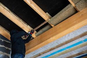 Worker Installing Insulation on Wooden Ceiling Framework photo