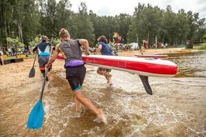 Group Carrying Red Paddleboard into Shallow Water at Beach Event photo