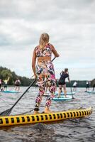Paddleboarders on Calm Water with Tree Lined Shoreline and Cloudy Sky photo
